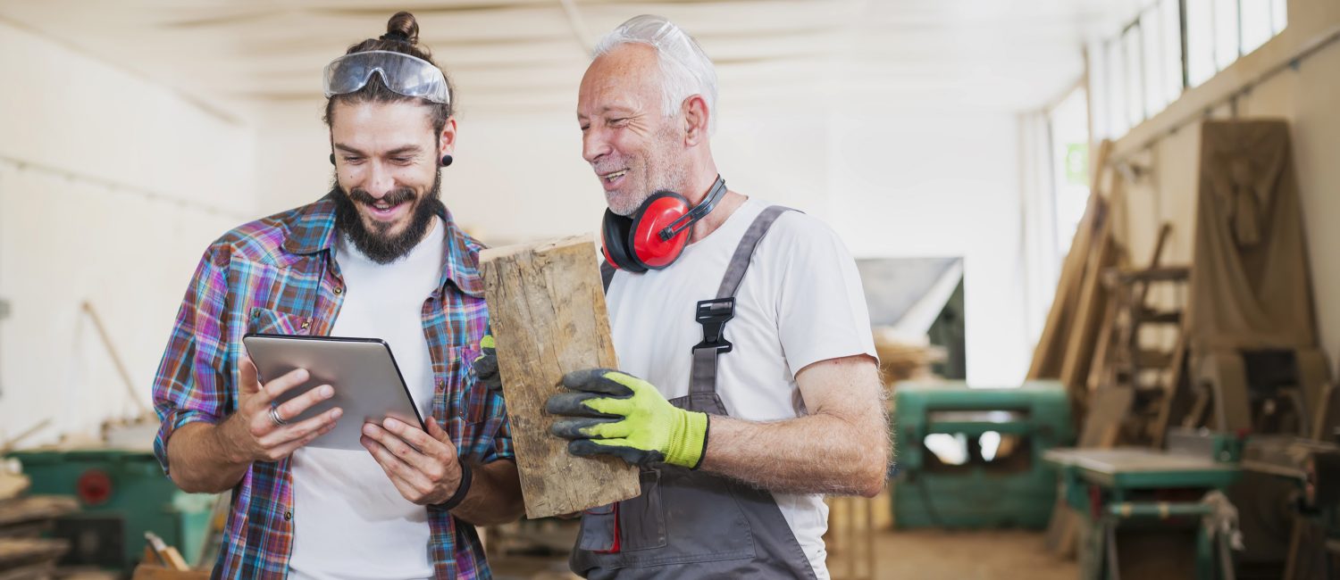 Carpenter’s at work Senior and young carpenter working at workshop using digital tablet